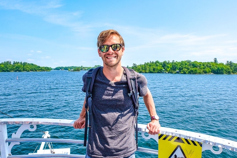 man in tshirt with sunglasses at front of boat and water behind on thousand islands cruise.