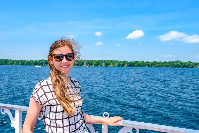 girl with sunglasses with white railing and blue water behind.