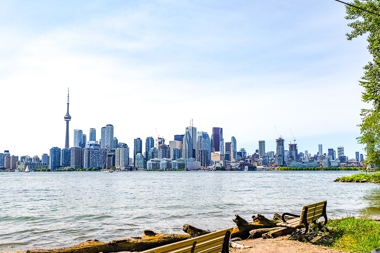 toronto buildings skyline with lake and benches in foreground.