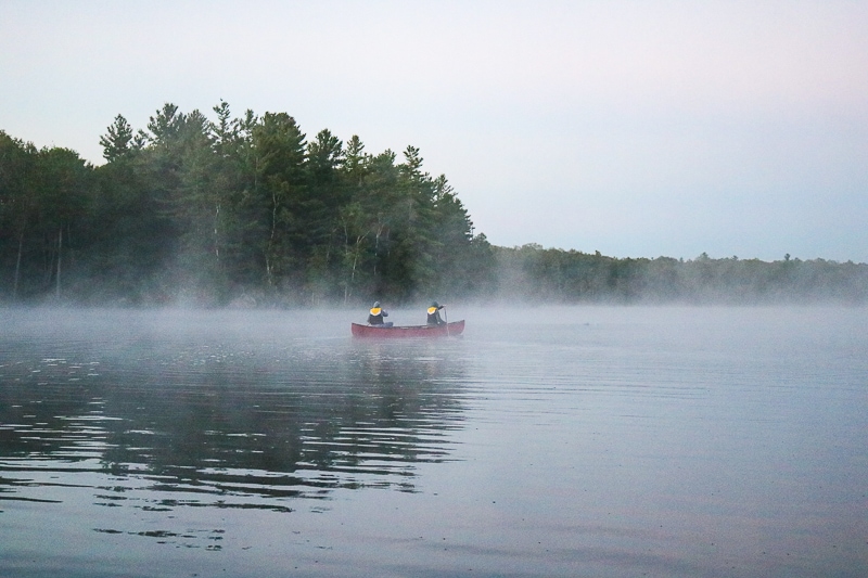 red canoe with two paddlers crossing misty lake.